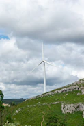 Technicians inspecting a modern wind turbine on a grassy hill.