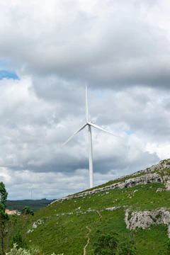 Technicians inspecting a modern wind turbine on a grassy hill.