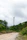 A tall wind turbine stands amidst a lush green landscape, surrounded by dense trees and foliage. A dirt path leads towards the turbine, under a cloudy sky that suggests an overcast day.