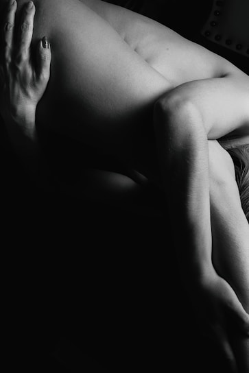 A black and white photograph features a person in an artistic pose, highlighting the contours and shadows of the human form. The lighting creates a dramatic effect, focusing on the texture and shape of the limbs.