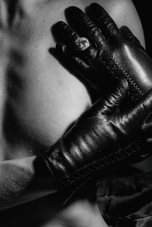 Close-up of stylish accessories: leather gloves, a silver collar, and a delicate yet commanding hand gesture.