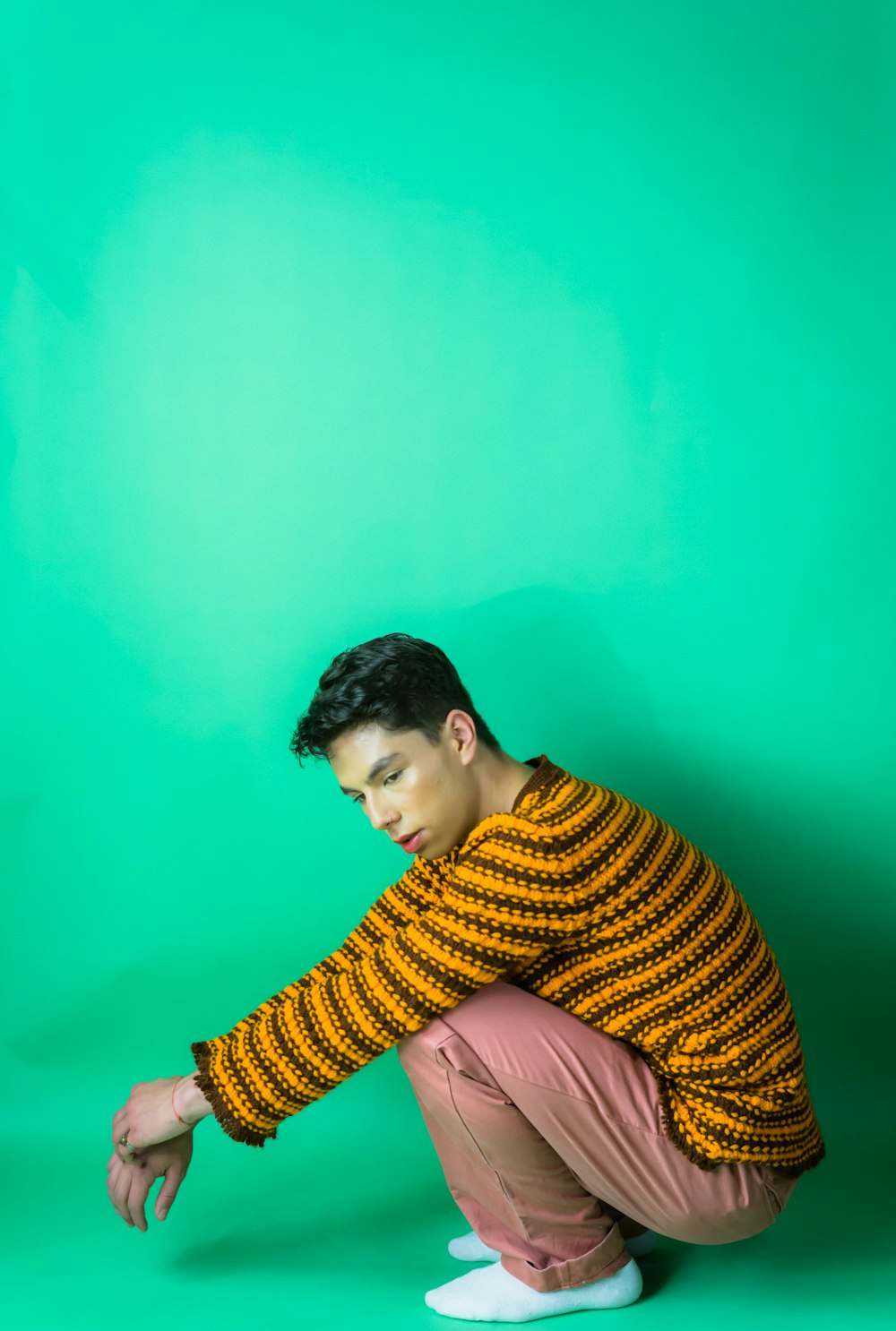 a young man squatting on a stool in front of a green background