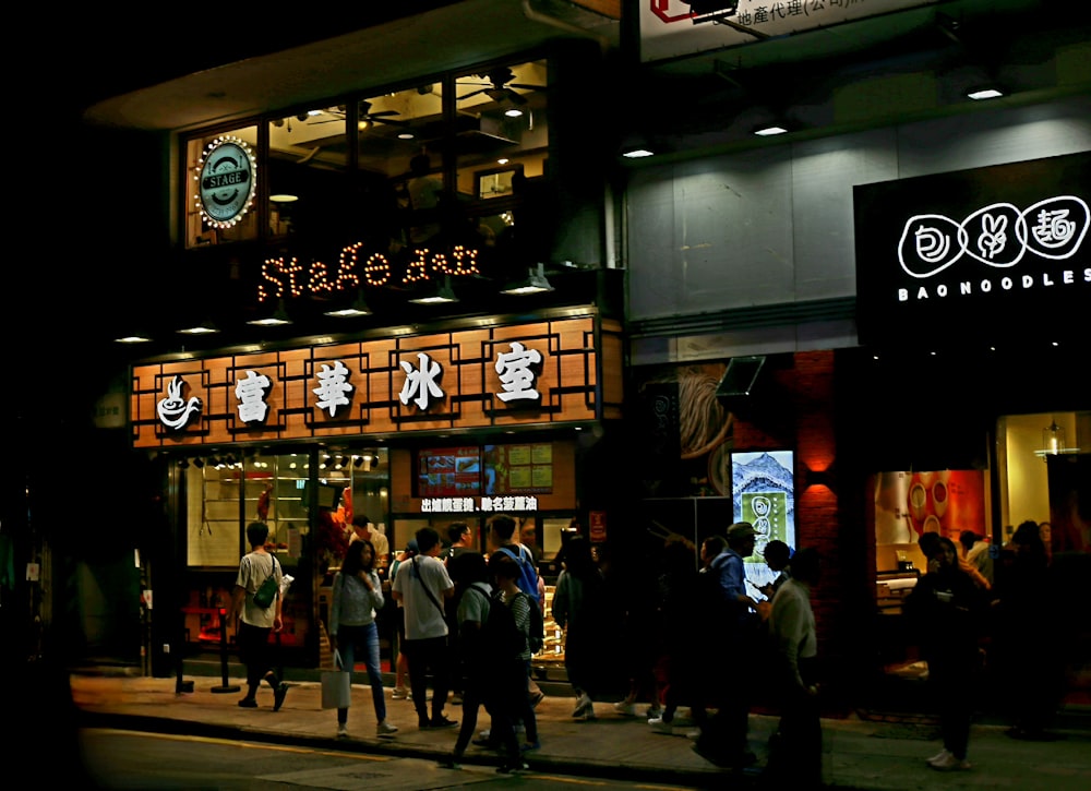 a group of people standing outside of a restaurant at night