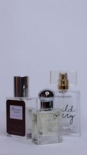Three perfume bottles are arranged closely together against a plain background. Each bottle has a unique design with varied labels and caps, showcasing different brands and styles.