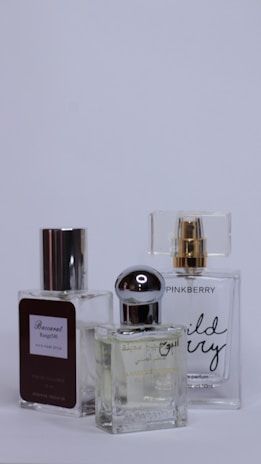 Three perfume bottles are arranged closely together against a plain background. Each bottle has a unique design with varied labels and caps, showcasing different brands and styles.