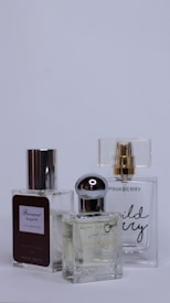 Three perfume bottles are arranged closely together against a plain background. Each bottle has a unique design with varied labels and caps, showcasing different brands and styles.