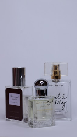 Three perfume bottles are arranged closely together against a plain background. Each bottle has a unique design with varied labels and caps, showcasing different brands and styles.
