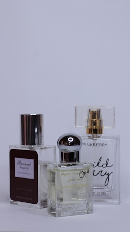 Three perfume bottles are arranged closely together against a plain background. Each bottle has a unique design with varied labels and caps, showcasing different brands and styles.