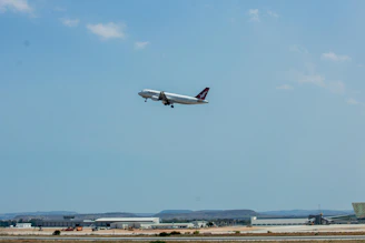 A sleek airplane taking off against a clear blue sky with cityscape below.