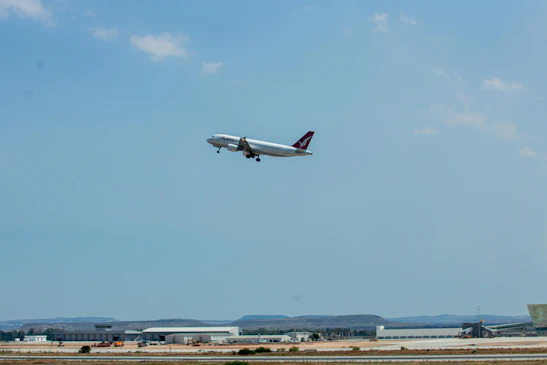 A sleek airplane taking off against a clear blue sky with cityscape below.