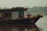 A small, rustic boat with a wooden and metal structure floats on a calm river. The boat is equipped with various objects like barrels, ropes, and fishing tools, and is covered with a tarp. The background features a misty, mountainous landscape with soft greenery.