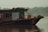 A small, rustic boat with a wooden and metal structure floats on a calm river. The boat is equipped with various objects like barrels, ropes, and fishing tools, and is covered with a tarp. The background features a misty, mountainous landscape with soft greenery.
