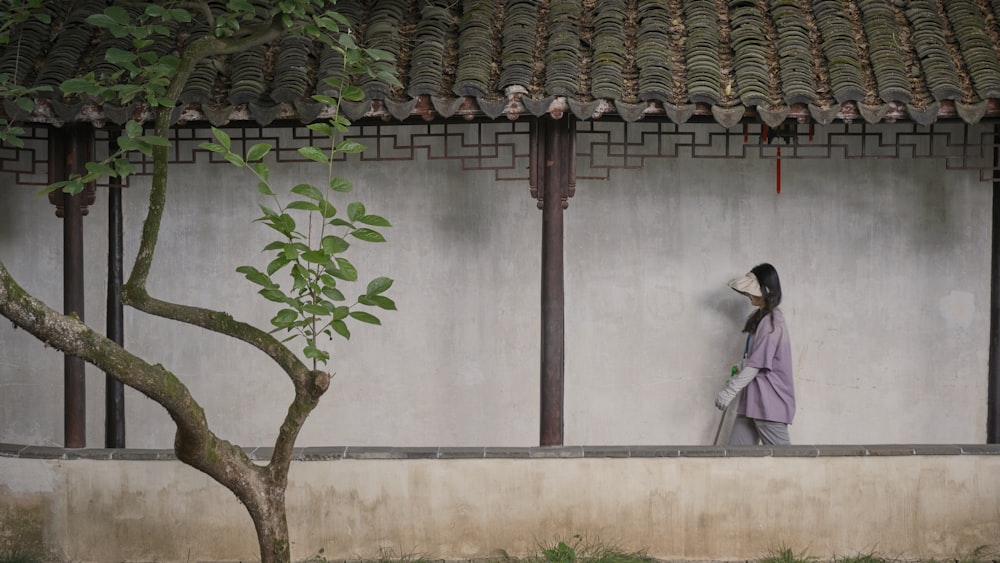 a woman standing next to a tree in front of a building