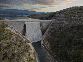 Water resource project featuring a large dam with water flowing through spillways and workers inspecting the site.