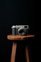 A minimalist black and orange themed photo of a camera on a wooden table with soft natural light.