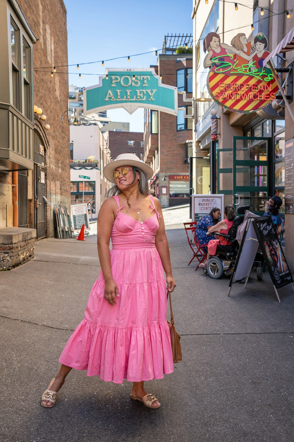 a woman in a pink dress and hat walking down a street