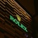 An illuminated sign with the brand name 'ROLEX' in green neon lights and a golden crown logo above, set against a dark, slatted background.