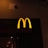 A prominently lit yellow 'M' logo on a dark background, characteristic of a well-known fast-food chain.
