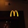 A prominently lit yellow 'M' logo on a dark background, characteristic of a well-known fast-food chain.