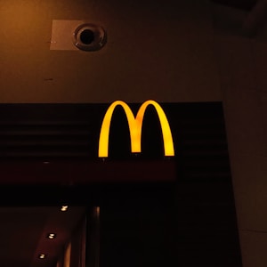A prominently lit yellow 'M' logo on a dark background, characteristic of a well-known fast-food chain.