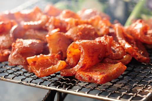 Close-up of a rich, smoky marinade being brushed over a sizzling grill with assorted meats.