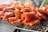 Sizzling pieces of marinated meat are cooking on a barbecue grill. The meat is well-seasoned with a rich, red marinade, and it's placed on a wire mesh grill. The background is slightly blurred, emphasizing the focus on the meat with hints of smoke rising