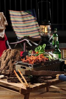 A wooden barbecue table set up with grilling tools and fresh ingredients ready for a cookout.