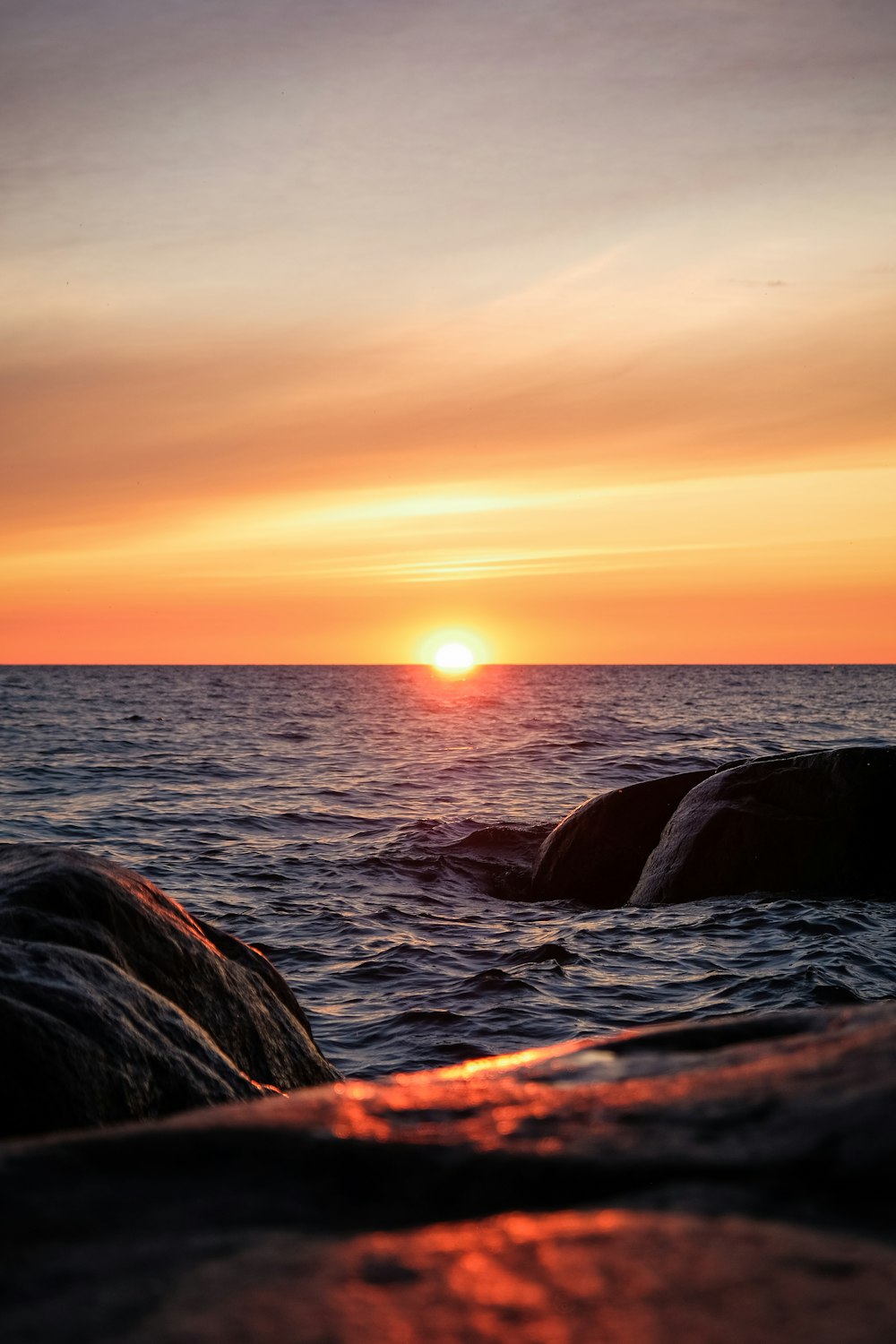 the sun is setting over the ocean with rocks in the foreground