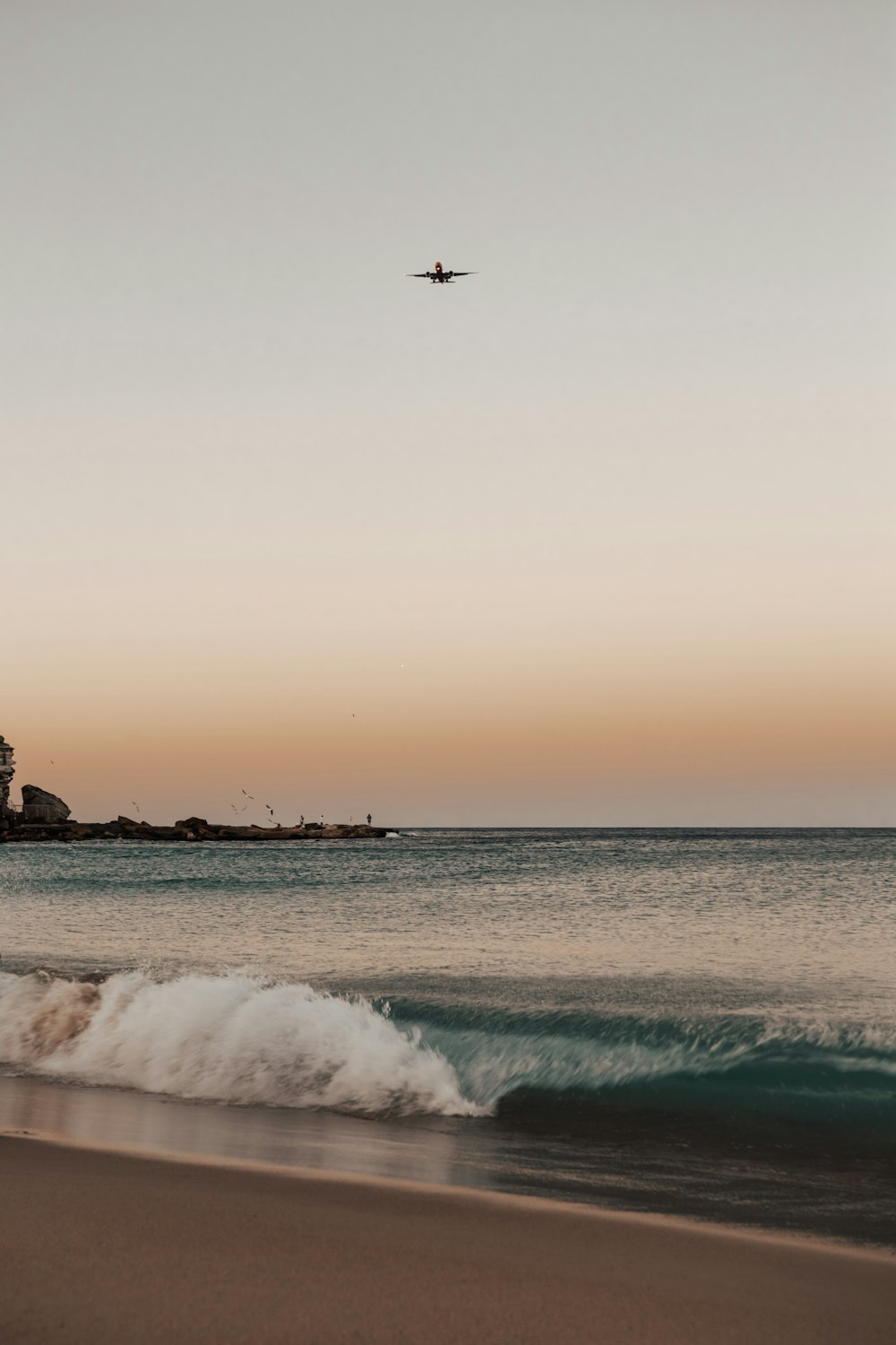 a plane flying over the ocean with a lighthouse in the background