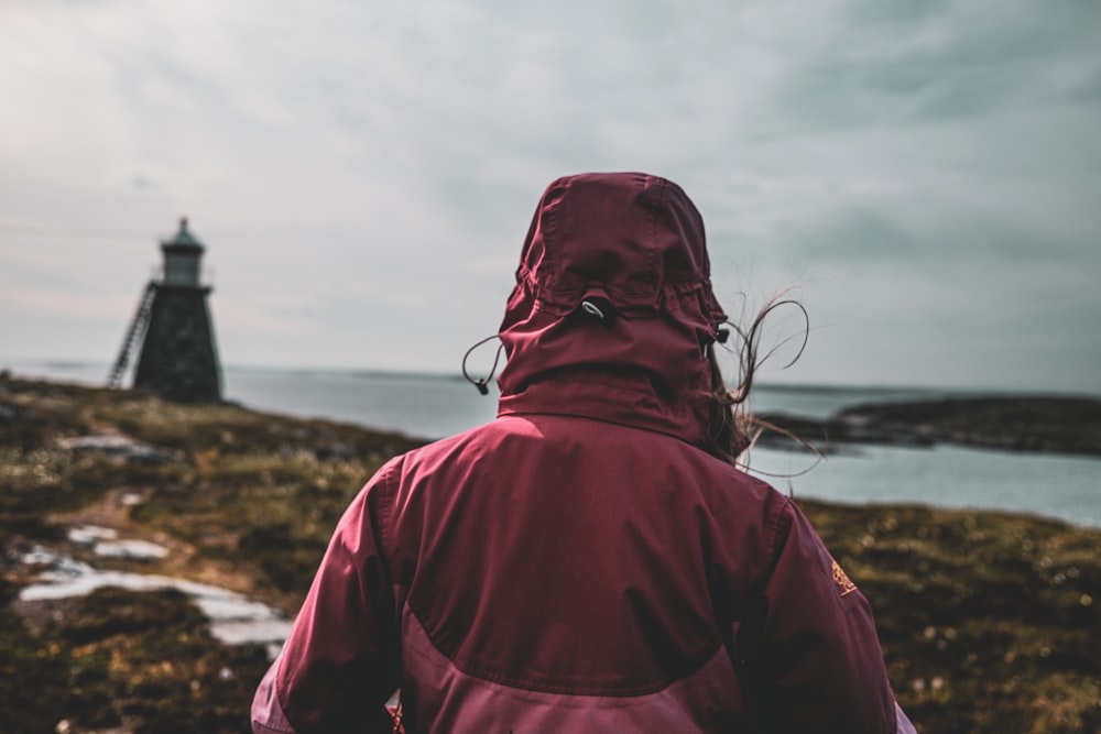 a person in a red jacket looking at a lighthouse