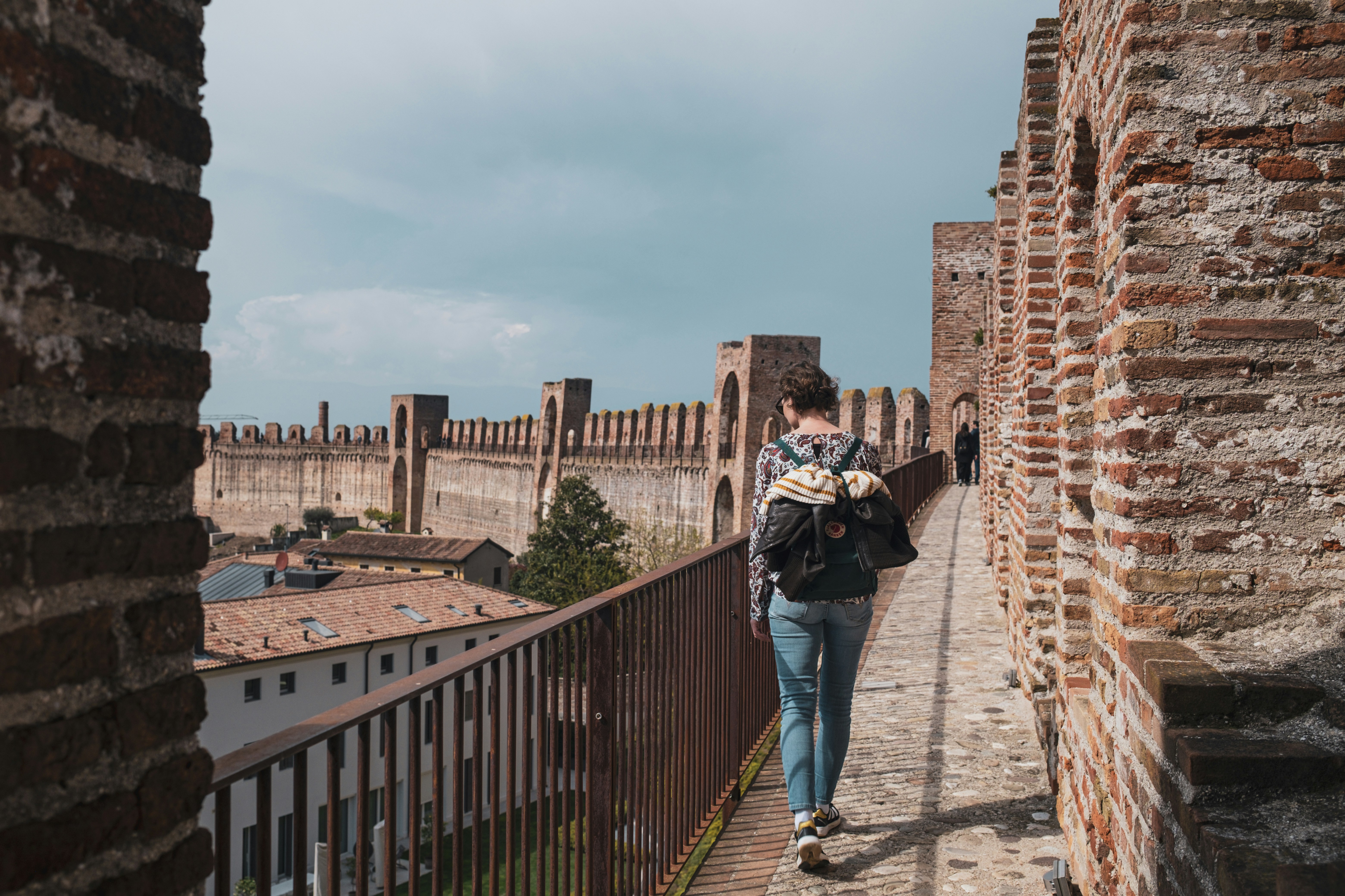 a man walking down a brick walkway next to a brick wall