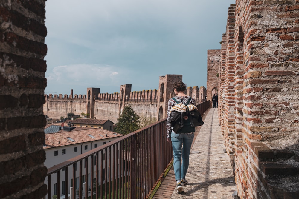 a man walking down a brick walkway next to a brick wall