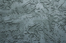 A textured surface with an irregular pattern of raised and recessed areas, resembling stucco or plaster. The surface has a rough, uneven texture with shadows enhancing the depth of the pattern.