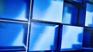Blue cubes with sharp edges are arranged in a geometric pattern, creating a three-dimensional effect with varying shades of blue and white highlights emphasizing depth and shadow.