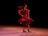 A dancer wearing a vibrant red dress twirls gracefully on stage. Her hair flows behind her as she spins, creating a sense of dynamic movement. The dark background makes the dancer stand out, highlighting the fluid motion and elegance of her performance.