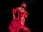 A joyful woman spinning effortlessly in a flowing red salsa dress under soft stage lights.