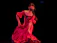A joyful woman spinning effortlessly in a flowing red salsa dress under soft stage lights.