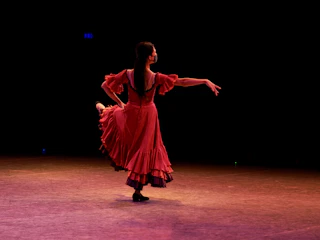 A vibrant flamenco dancer in colorful traditional attire performing on stage with dynamic lighting.