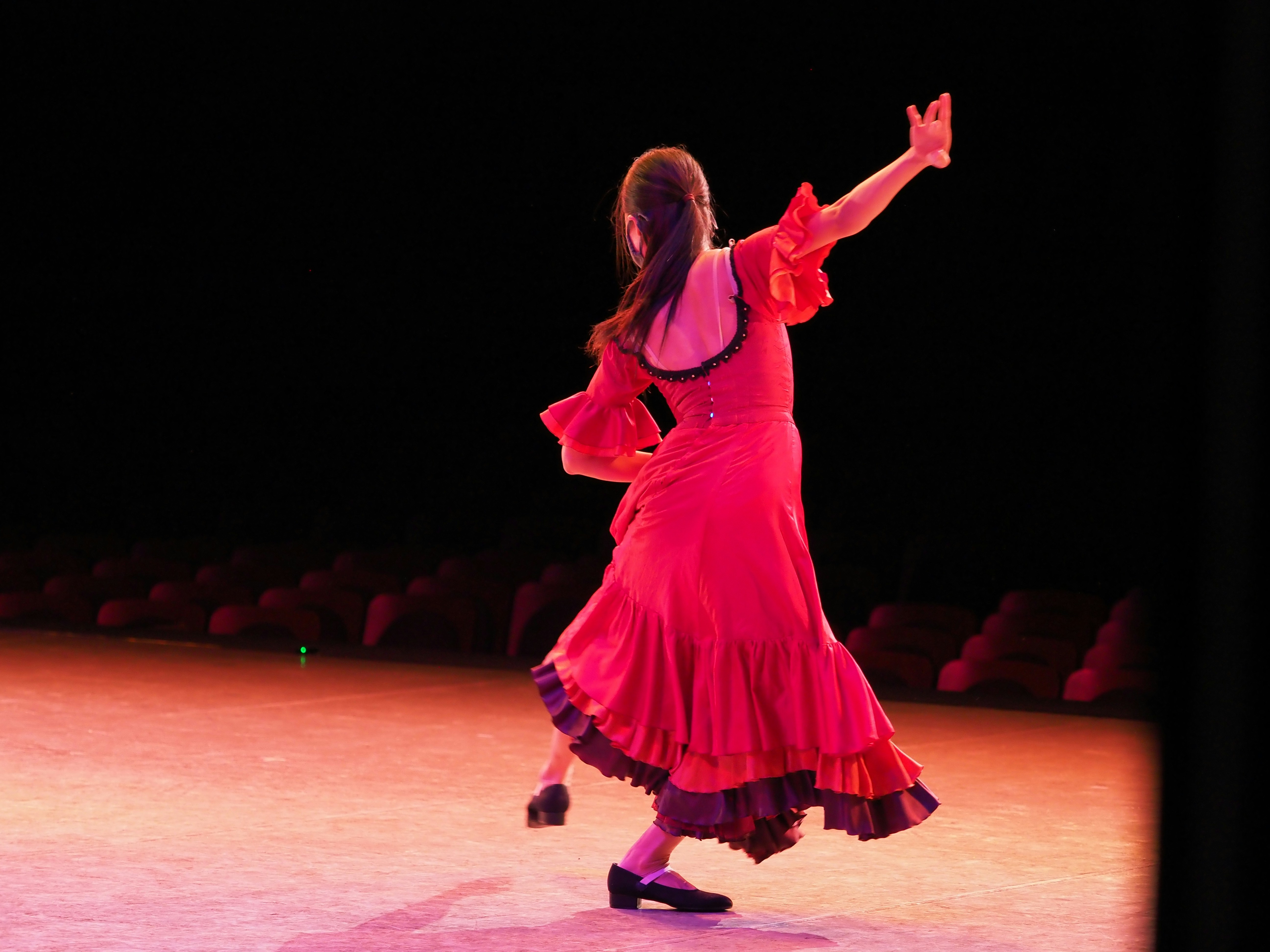 Flamenco dancer in red dress performing on stage, dramatic spotlight, dark theatrical background
