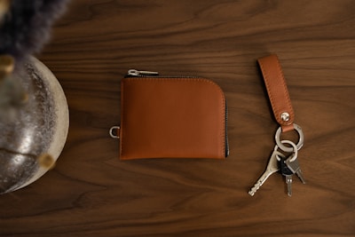 A stylish leather wallet and matching keychain set on a dark wooden surface with gold accents