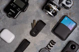 Flat lay of an airport travel carry setup featuring a minimalist wallet, keys, phone, and boarding pass on a charcoal surface.