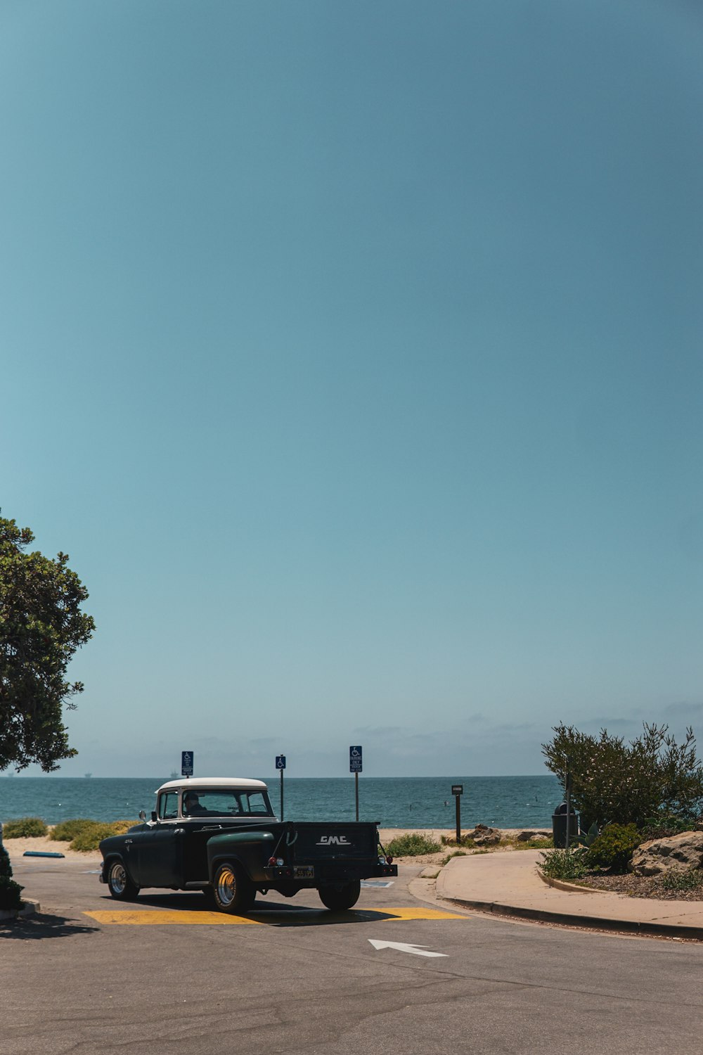 a black truck driving down a street next to the ocean