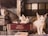 Two cats are resting on top of stacked books, with a focus on one cat lying on a red book titled 'Evidence.' The background includes a gridded window and a beige chair.