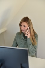 a woman sitting in front of a computer talking on a cell phone