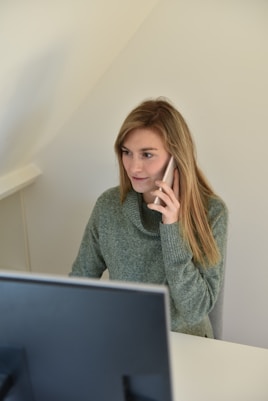 a woman sitting in front of a computer talking on a cell phone