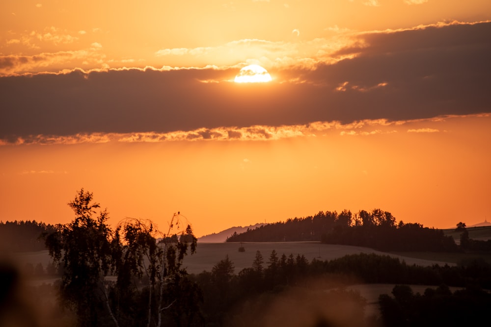 the sun is setting over a field with trees