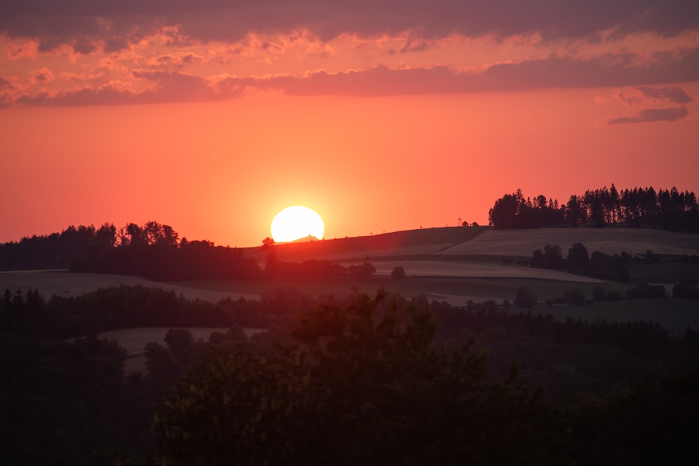 the sun is setting over a field with trees