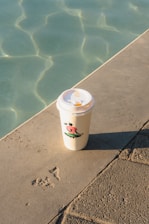 a cup of coffee sitting on the edge of a pool