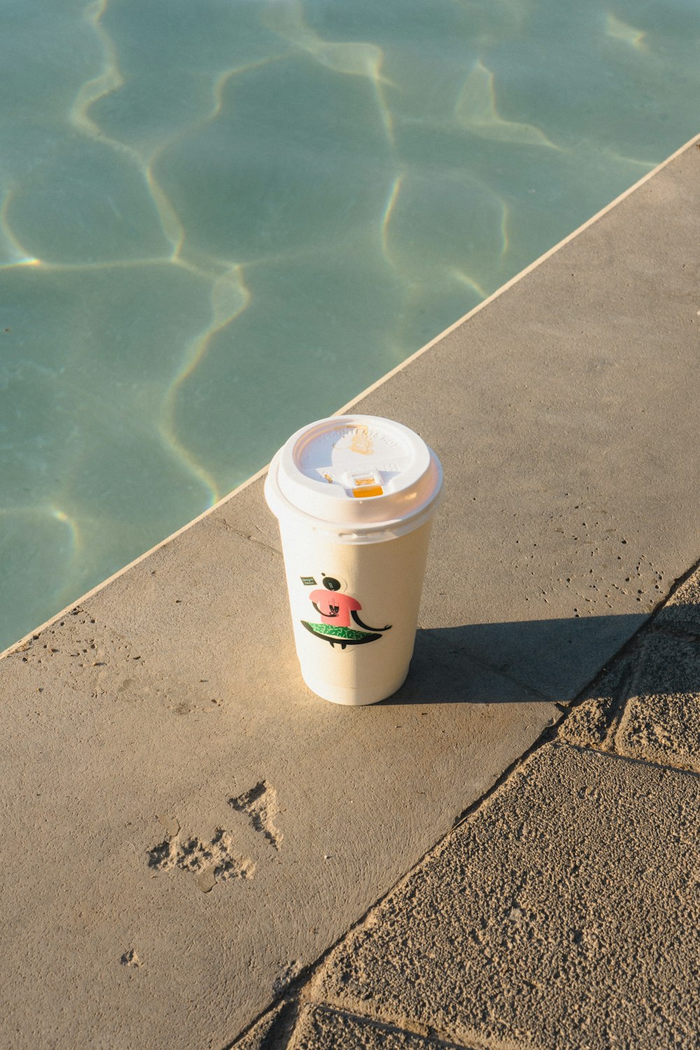 a cup of coffee sitting on the edge of a pool