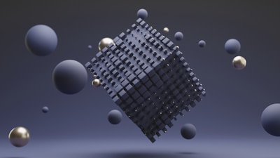 A geometric abstract scene featuring a large abstract cube made from many small dark squares, floating in space. Surrounding the cube are several spheres of varying sizes in shades of blue and metallic gold. The background is a smooth gradient of dark blue tones, enhancing a sense of depth.